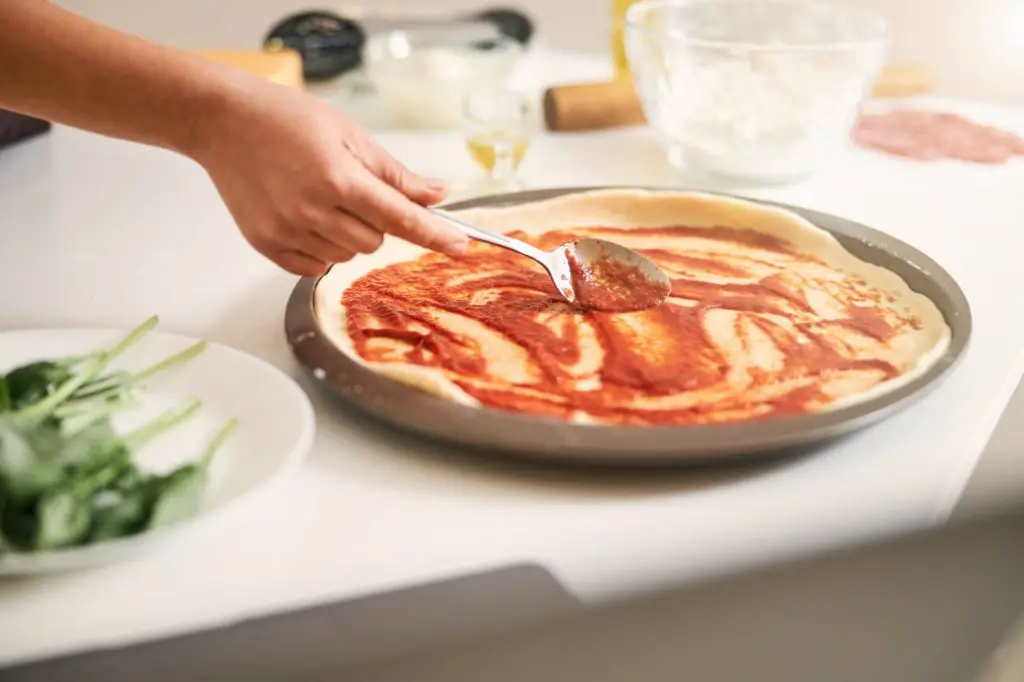 Covering the pizza base with tomato sauce