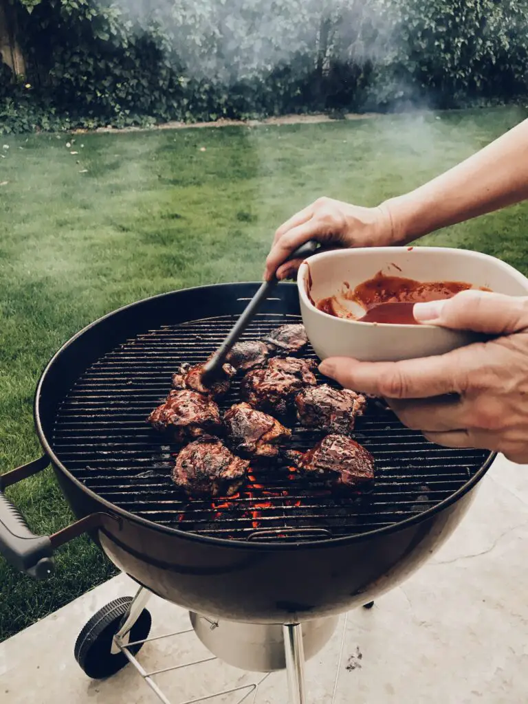Basting chicken on a smoky barbecue grill in a quiet green beautiful backyard