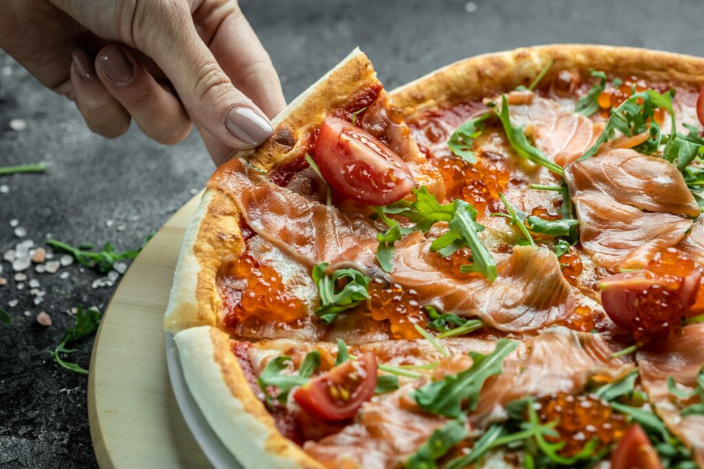 Female hands holding delicious pizza with salmon, red caviar, tomatoes and aragula. italian pizza
