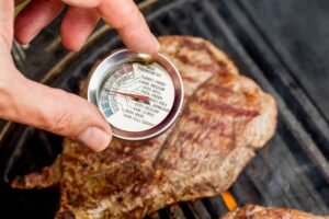 Grilled meat on bbq with hand holding meat cooking thermometer to check if steak is ready.