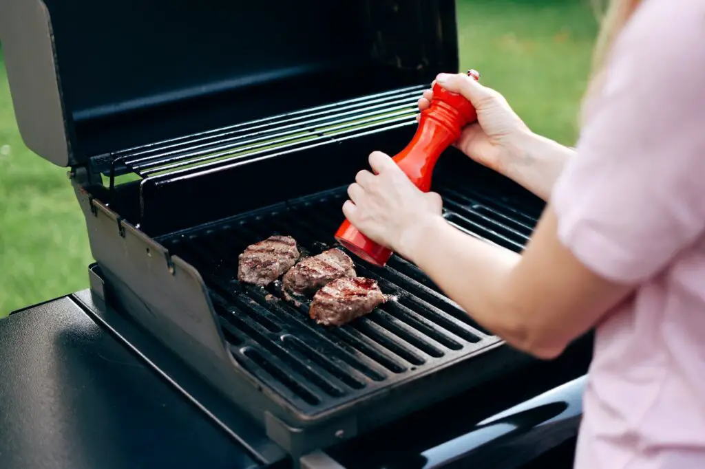 Side view of woman using pepper grinder to season steak on the grill
