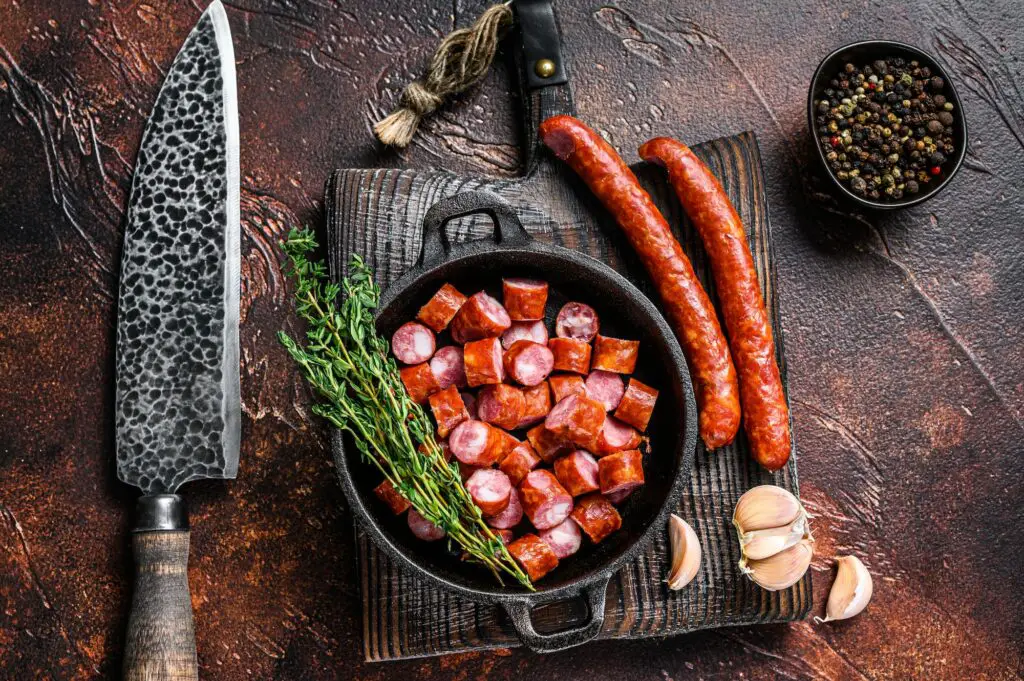 Sliced Hot Smoked sausages with aromatic herbs and spices. Dark background. Top view
