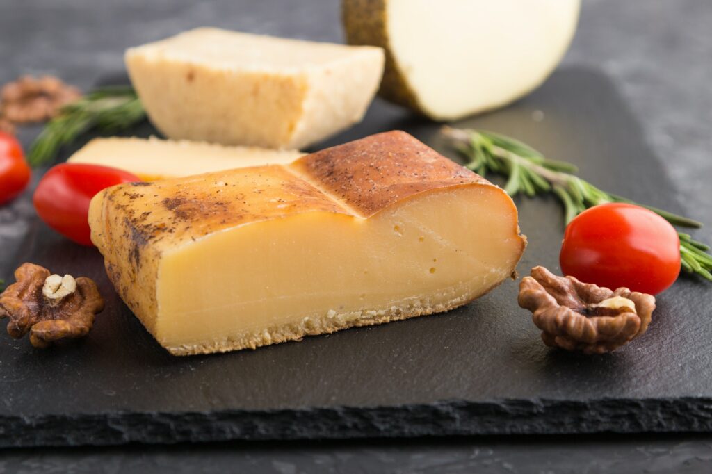 Smoked cheese and various types of cheese with rosemary and tomatoes on black slate board