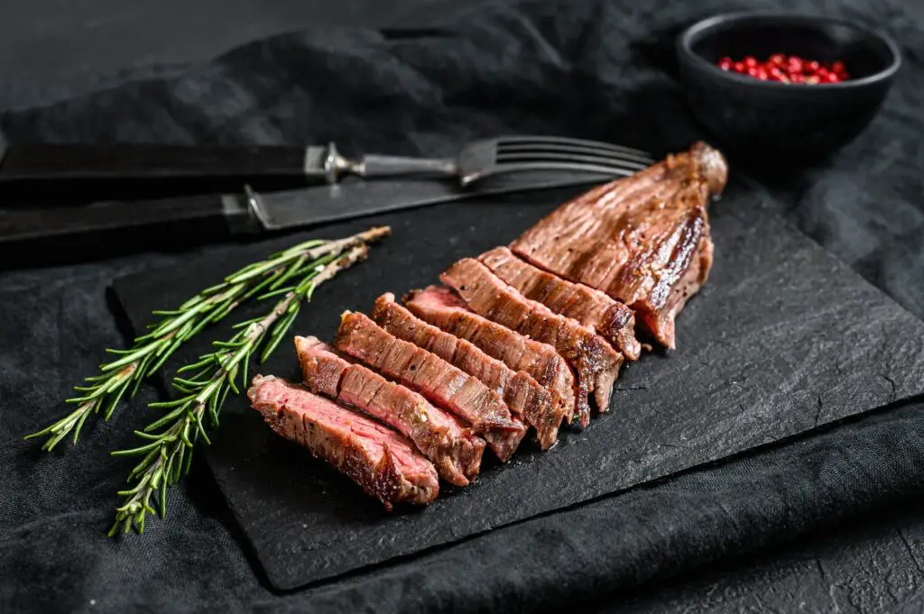 Sliced beef flank steak medium rare. Black background. Top view
