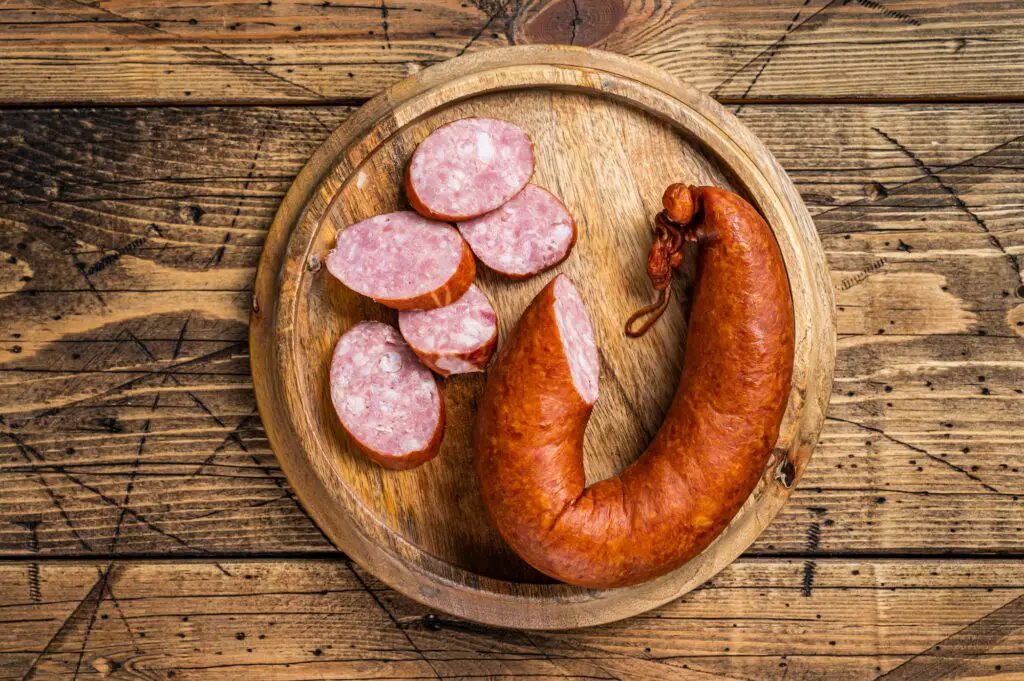Bavarian Smoked sausage on a wooden board with herbs. White wooden background. Top view